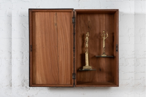 A wooden box hanging on a wall, with trophies inside